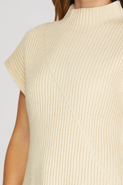 Close-up of a cream-colored ribbed knit top with short sleeves and a mock neck, worn by a model.
